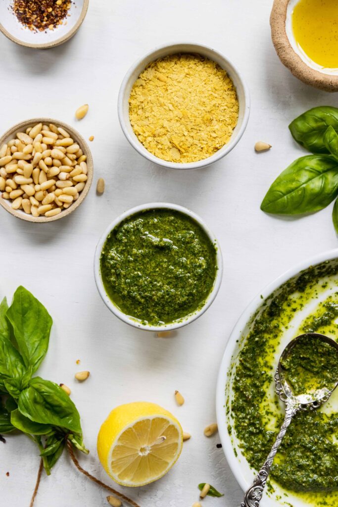 Vegan basil pesto served in a white bowl with fresh basil and pine nuts