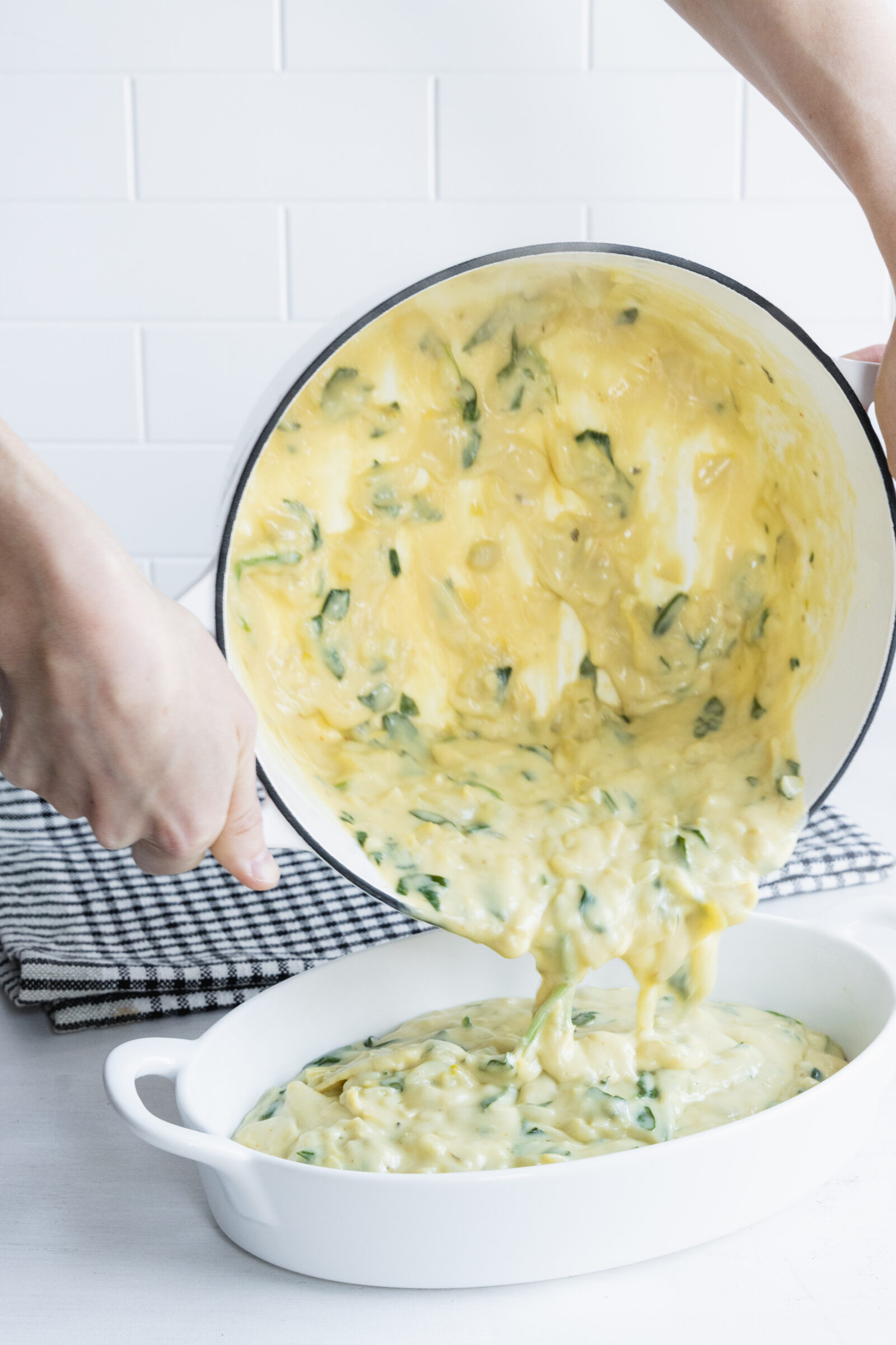 Pouring vegan spinach artichoke dip into a baking dish