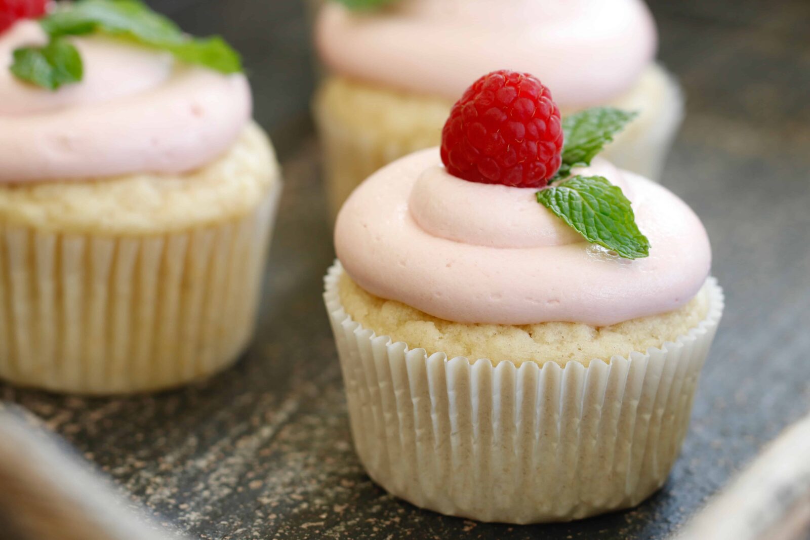 Vegan cupcakes with raspberry frosting. Garnished with a raspberry and mint leaves.