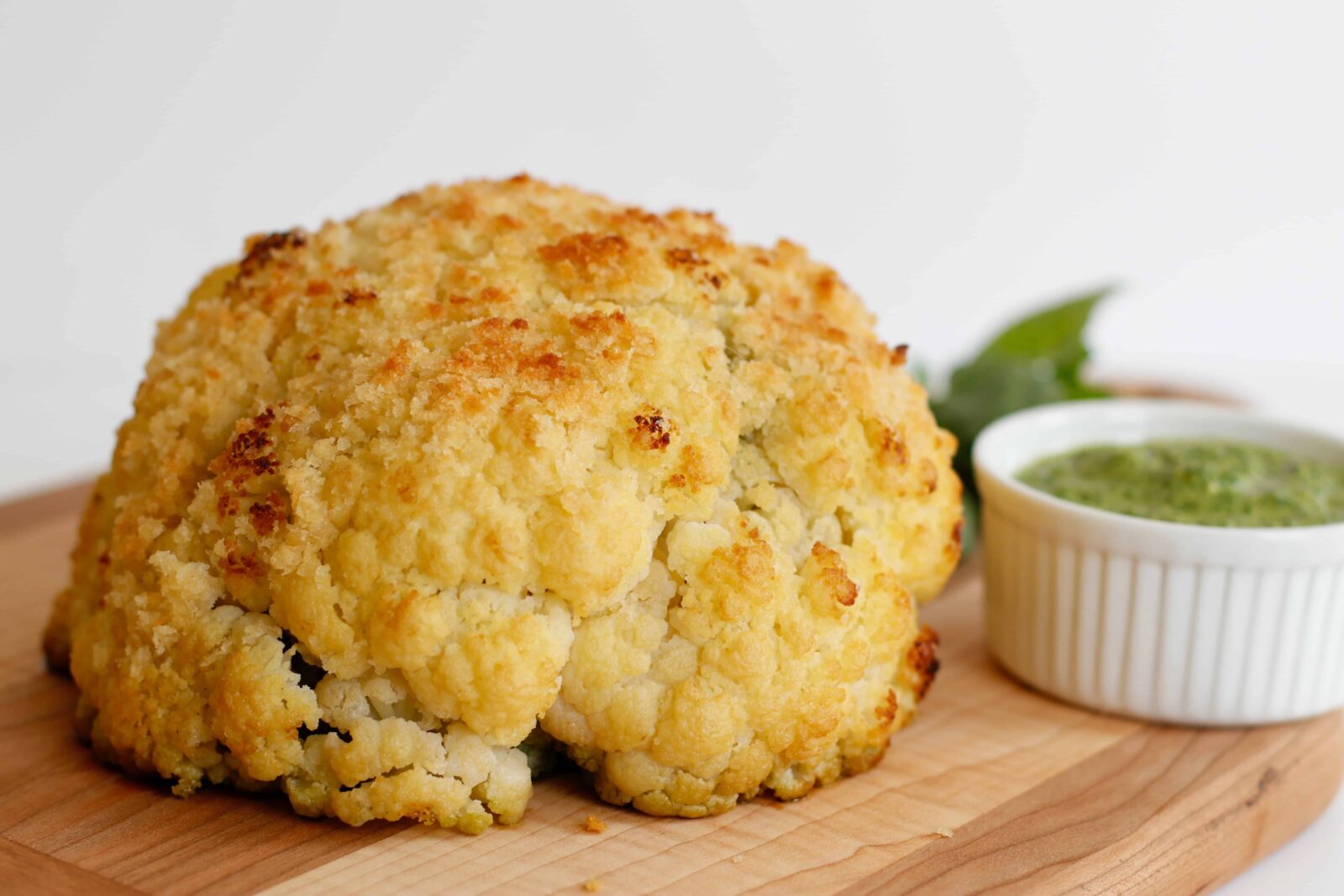 Whole Roasted Cauliflower, Stuffed With Pesto served on a wooden cutting board