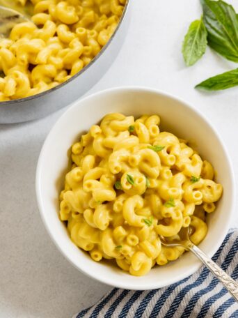 Vegan mac and cheese served in a white bowl and garnished with fresh basil leaves