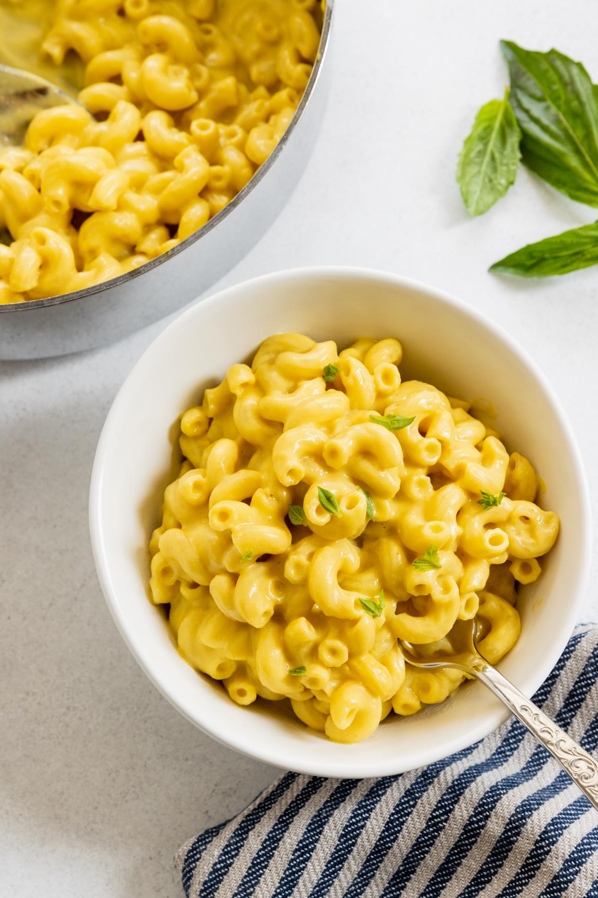 Vegan mac and cheese served in a white bowl with fresh basil leaves