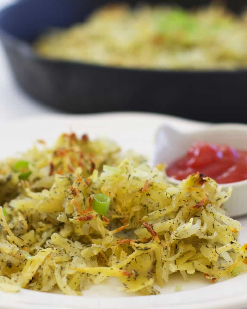 Hash browns with dill served on a white plate with ketchup. 