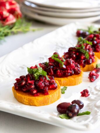 Roasted Sweet Potato Slices with Fresh Cranberry and Pomegranate Relish Served on a White Plate