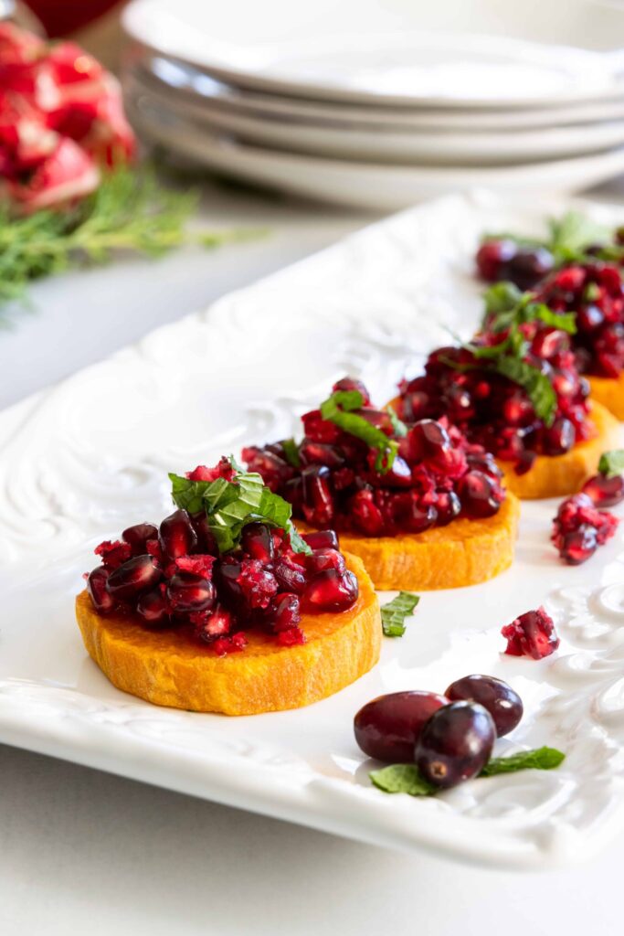 Roasted Sweet Potato Slices with Fresh Cranberry and Pomegranate Relish Served on a White Plate