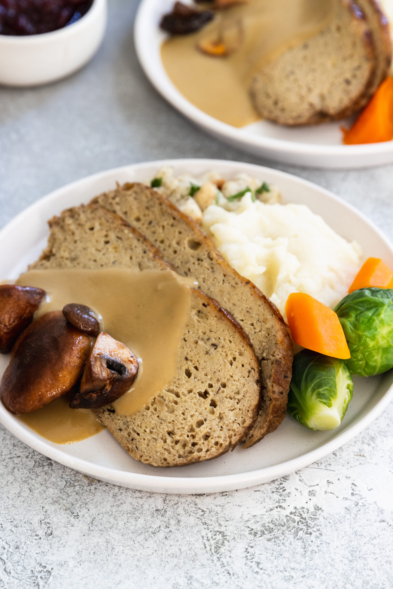 Two slices of vegan turkey roast served on a plate with mashed potatoes and vegan gravy