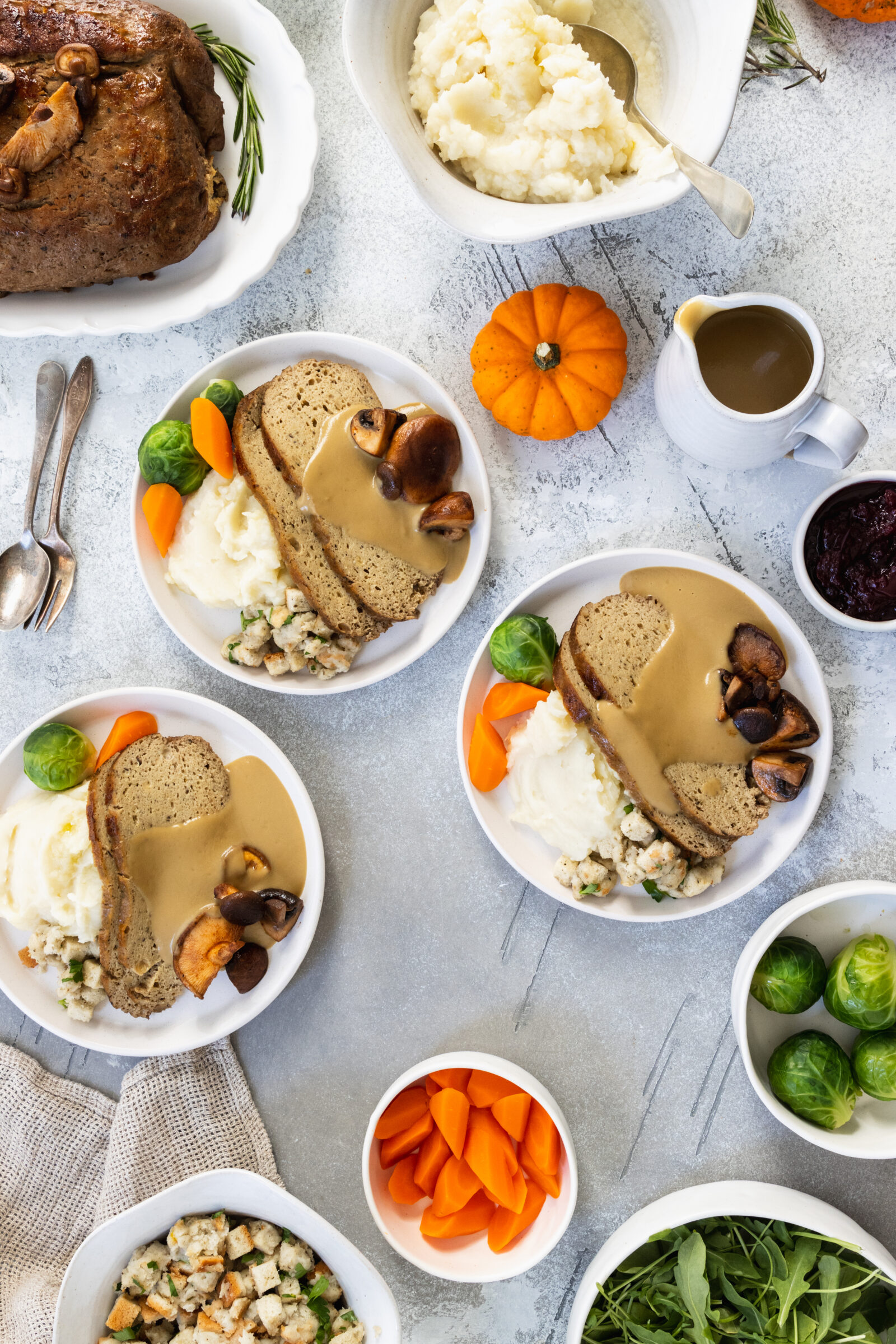 Three plates with vegan turkey roast, mashed potatoes, vegan gravy, and vegetables