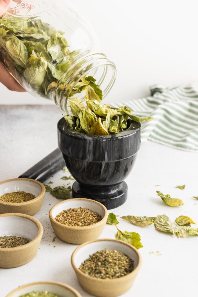 Pouring dried basil leaves in a mortar and pestle