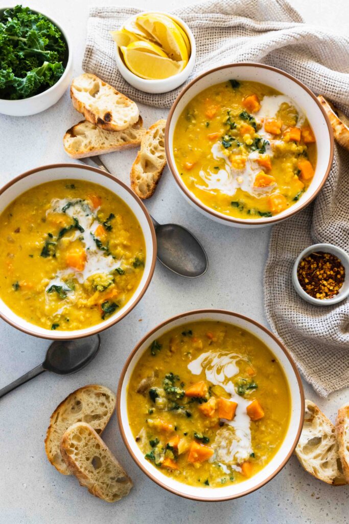 Sweet potato red lentil soup served in three bowls with crusty slices of bread