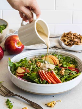 Pouring maple walnut dressing on the apple walnut salad in a white bowl