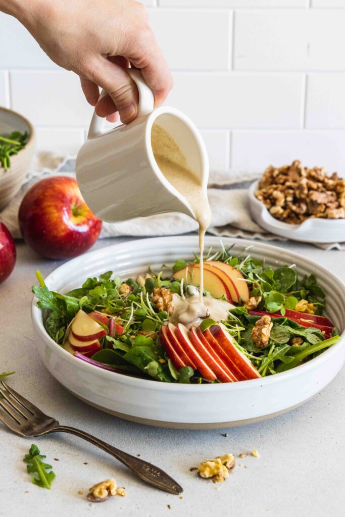 Pouring maple walnut dressing on the apple walnut salad in a white bowl