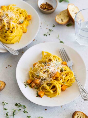 Roasted butternut squash pasta served on white plates with slices of crusty bread