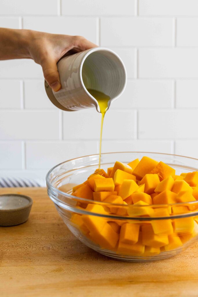 Pouring a drizzle of olive oil over the butternut squash