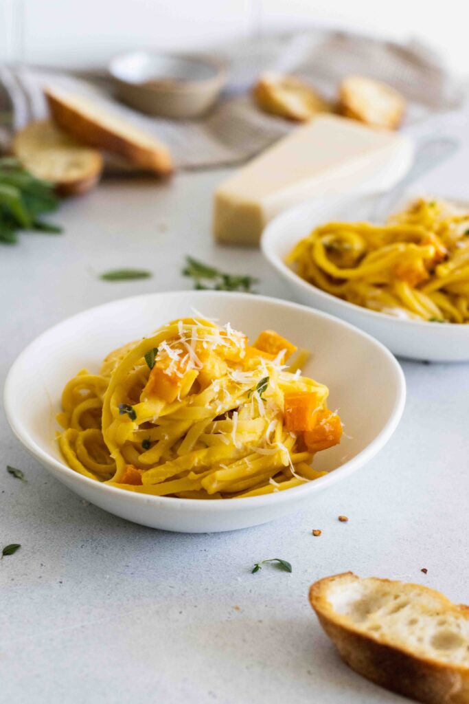 Roasted butternut squash pasta served in two bowls with vegan parmesan