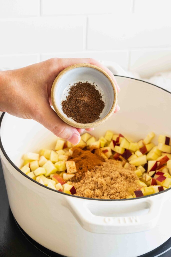Adding allspice to the apple mixture in a pot
