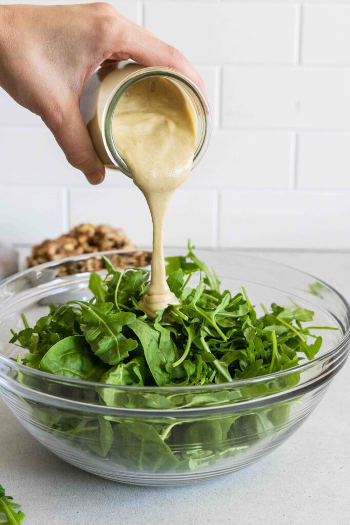 Pouring maple walnut dressing on salad greens
