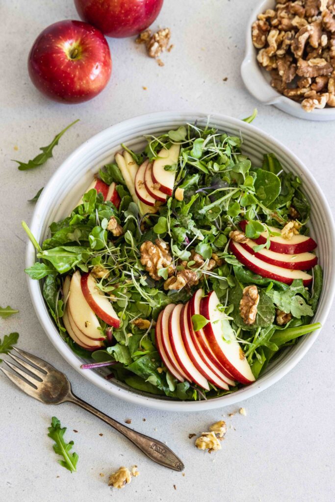 Apple walnut salad in a white bowl with sliced apples and toasted walnuts