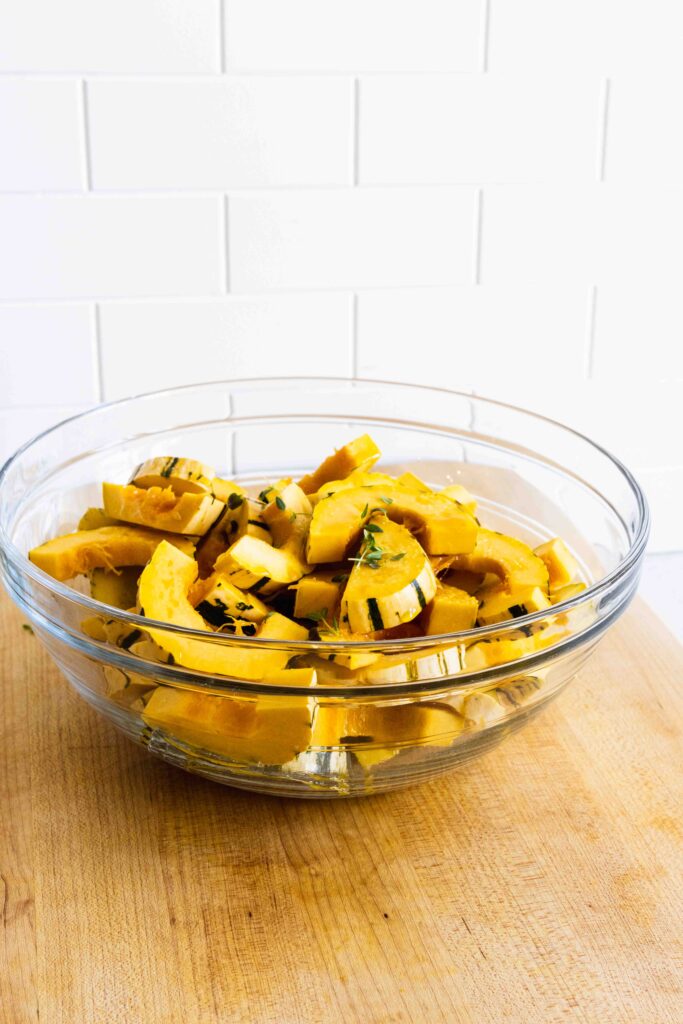 Adding fresh thyme leaves to the delicata squash in a bowl