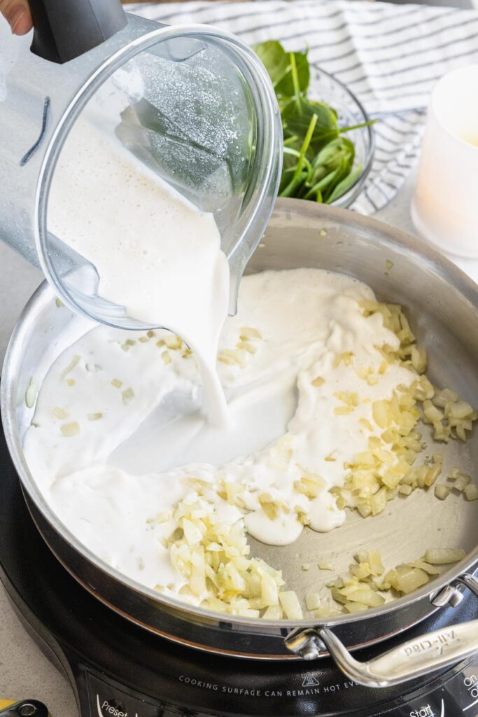 Pouring the vegan cashew cream into the onion and garlic mixture