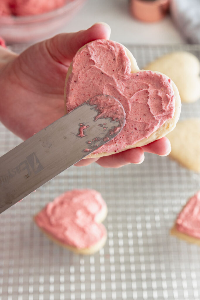 Frosting a soft vegan sugar cookie with strawberry frosting