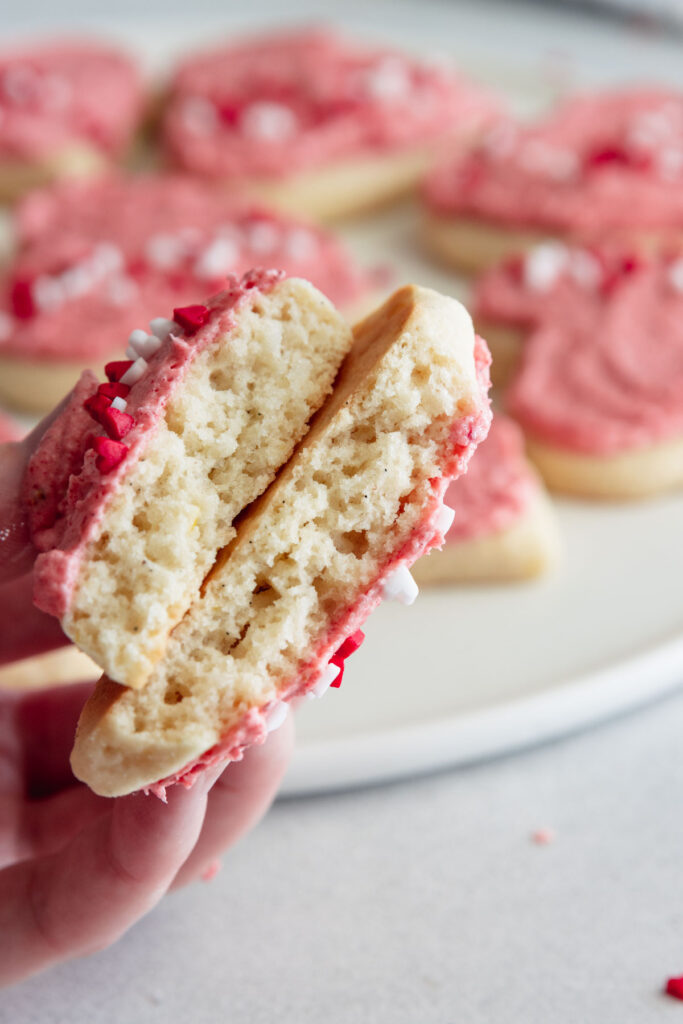 A soft frosted sugar cookie broken in two to show the interior of the cookie